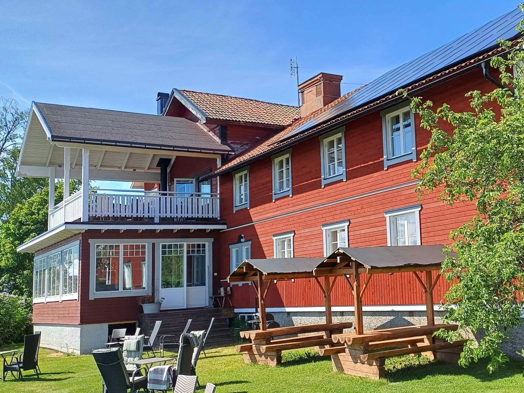 Red wooden house with porch, flowering trees and outdoor furniture on the lawn.
