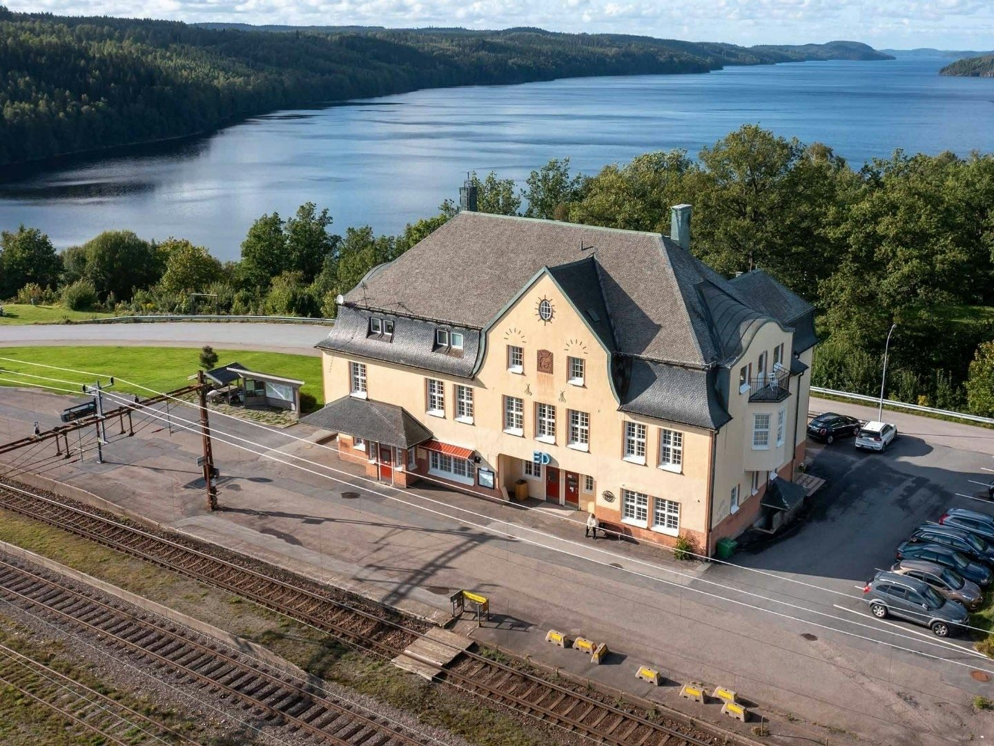 Stationshuset i Ed precis vid ett tågspår och med en sjö i bakgrunden. 