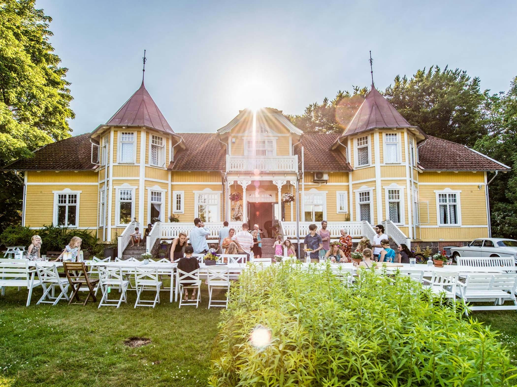 Gul träbyggnad i sekelskiftesstil med trädgårdsfest i kvällssolens sken.