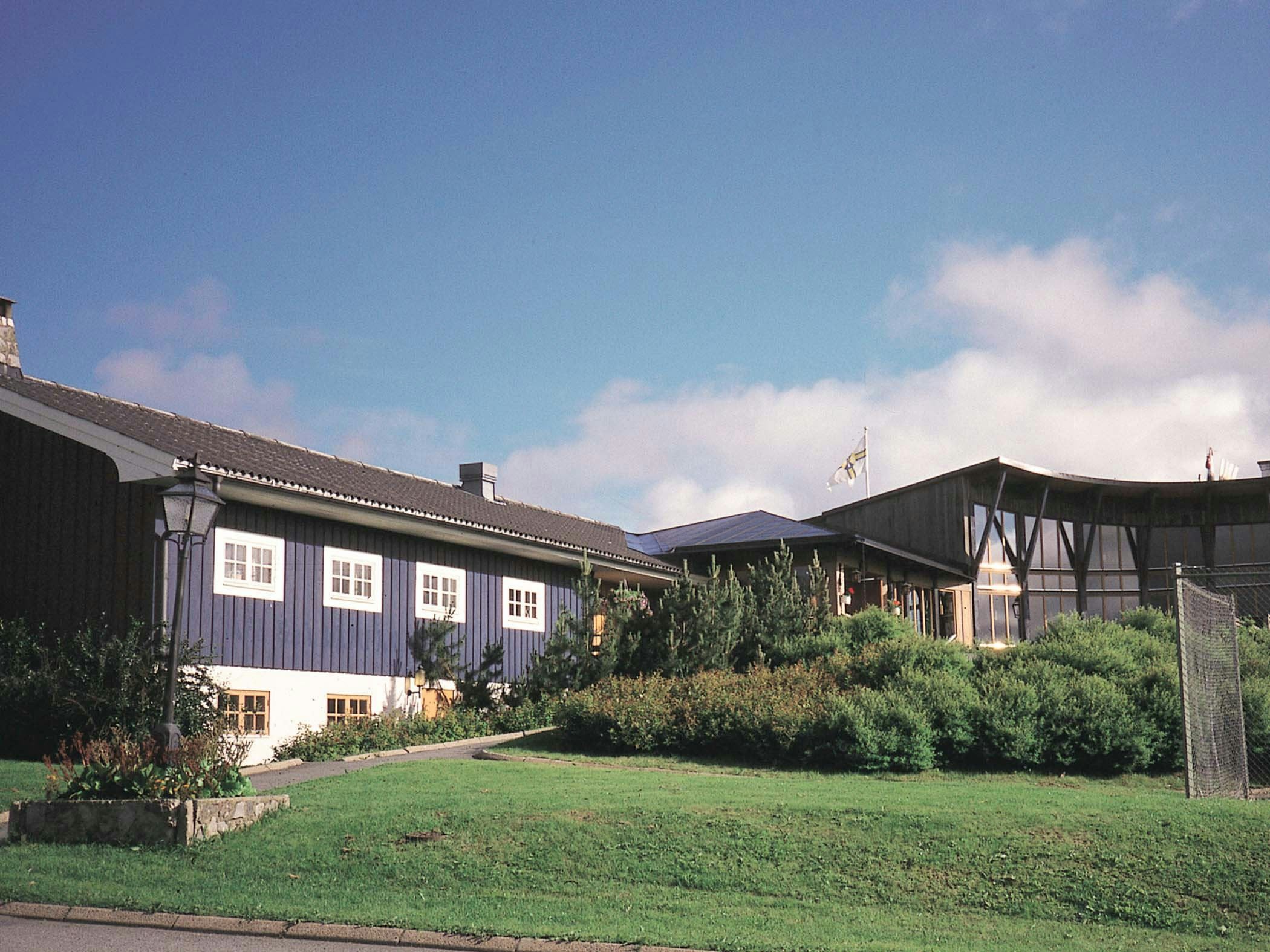 Blå hotellbyggnad med skyltar och välskött grönområde.