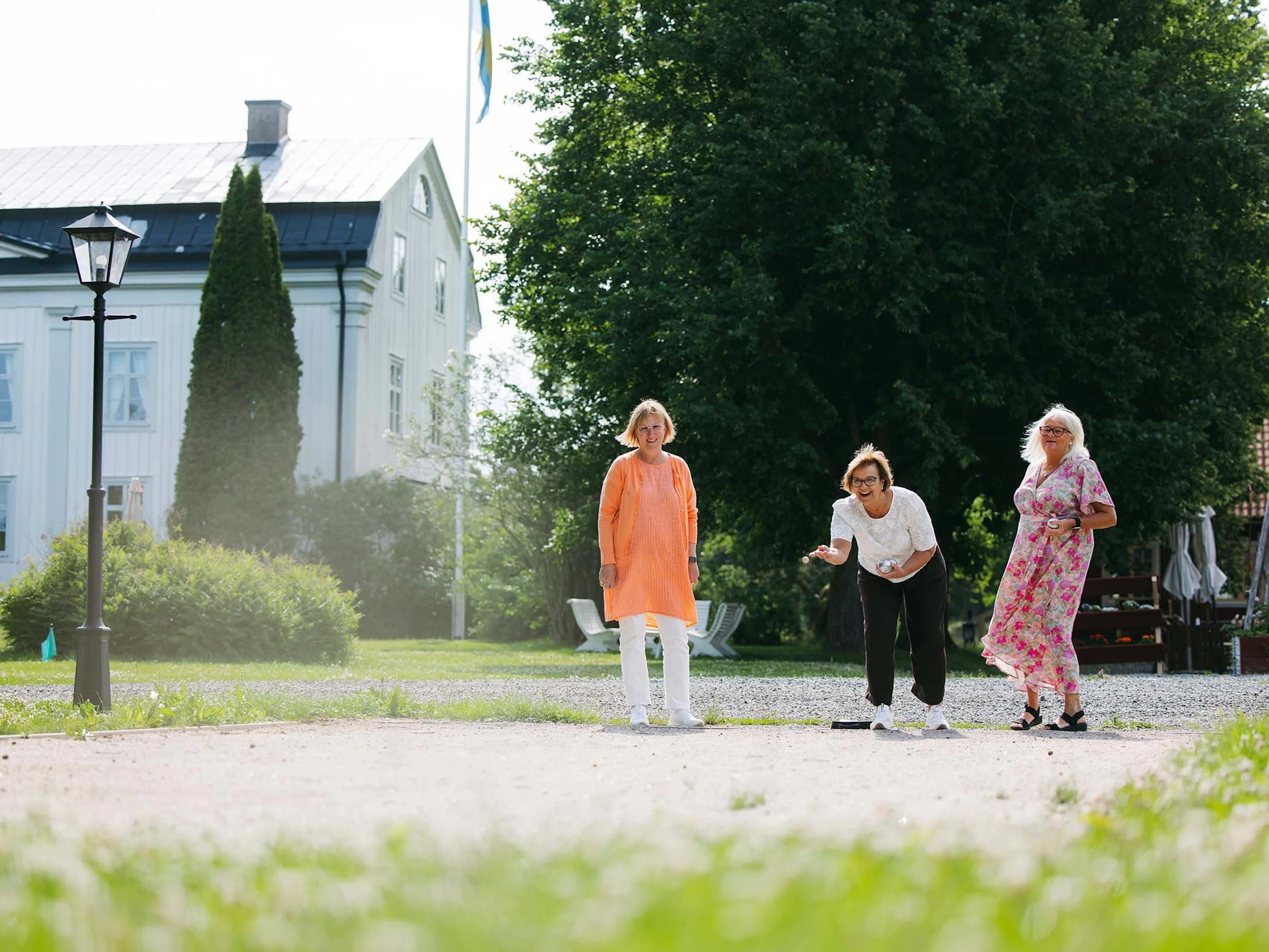 Tre kvinnor spelar boule framför herrgården på Wallby Säteri.