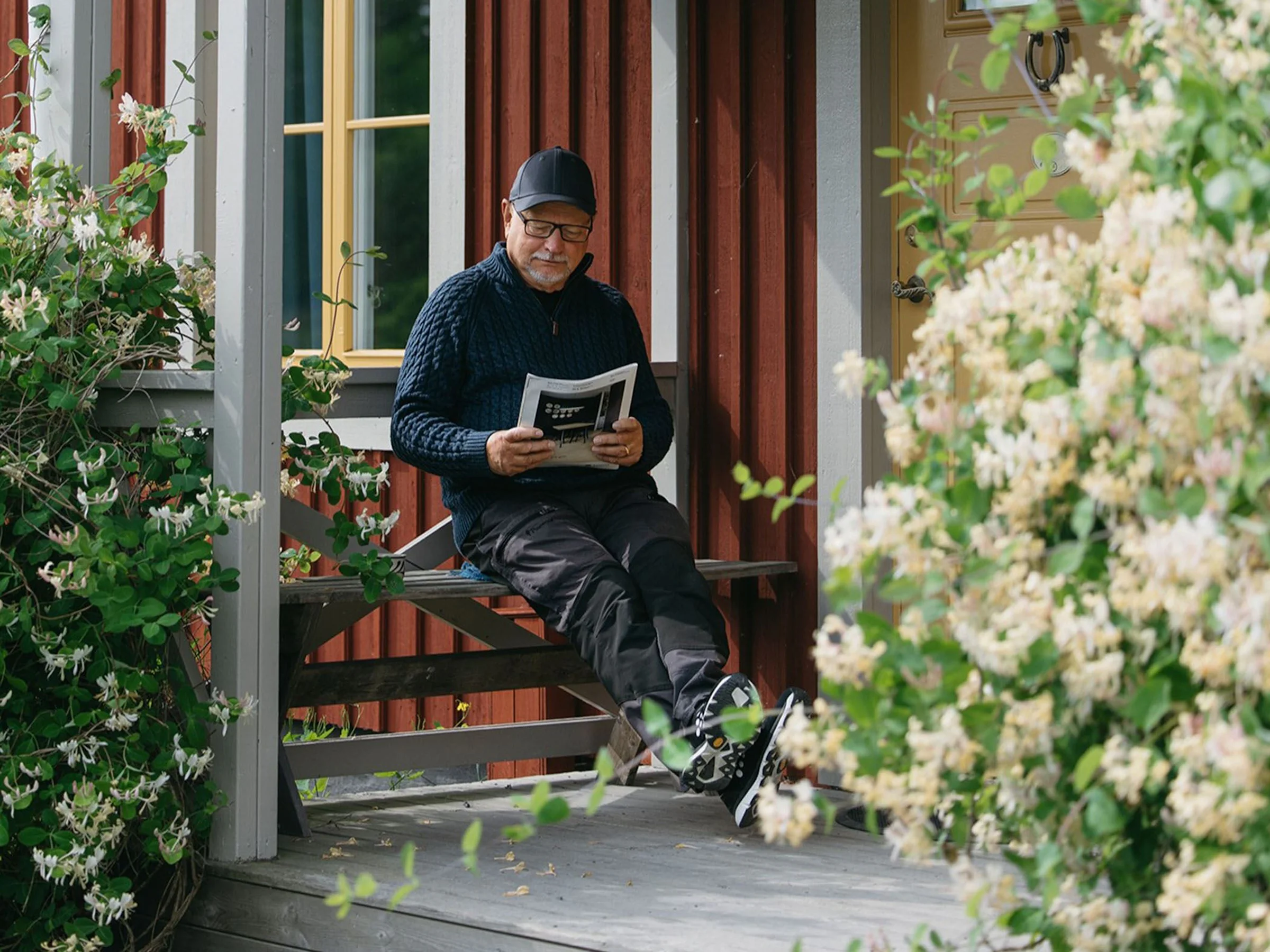 Man läser en tidning på en blomsterkantad veranda.