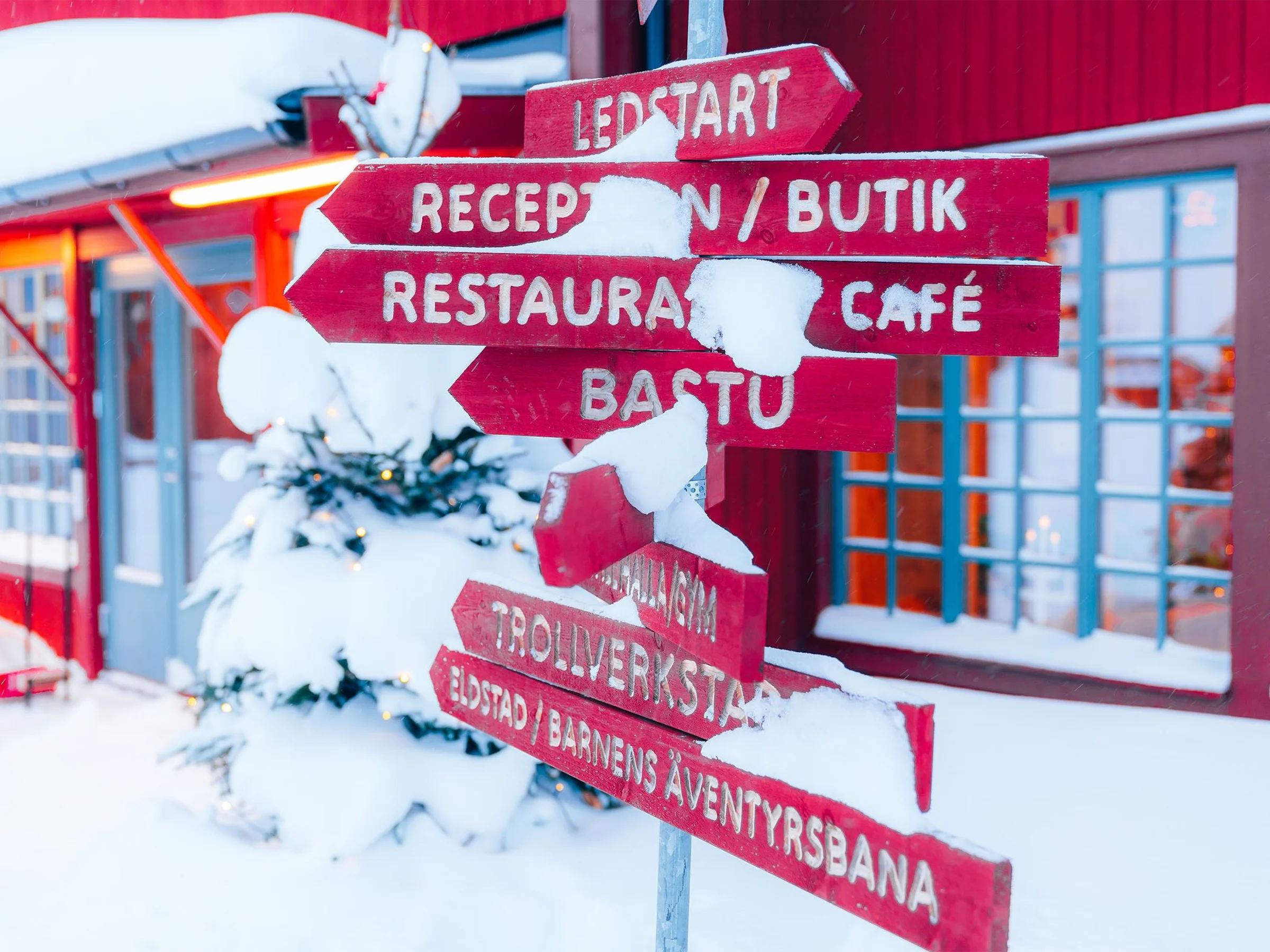 Red signposts in the snow by a red building.