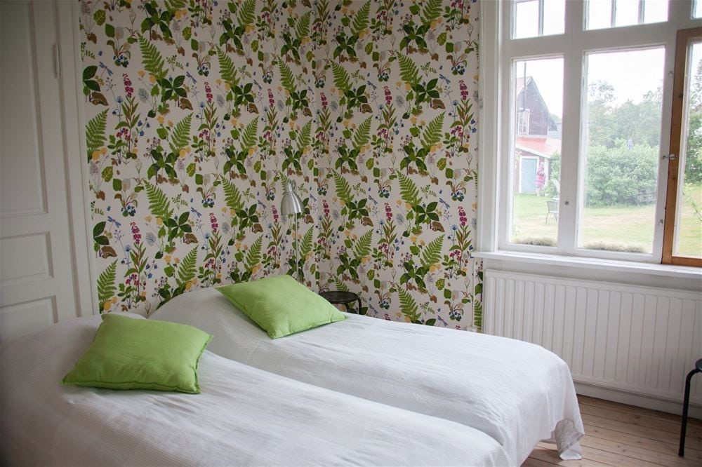Bright bedroom with floral wallpaper, two beds and green pillows against the window.