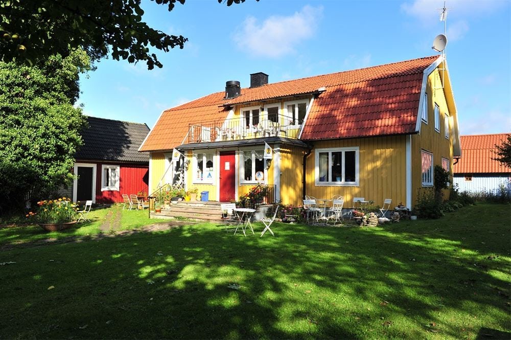 Yellow wooden villa with red tiled roof, green garden with garden furniture, blue sky and sunshine.