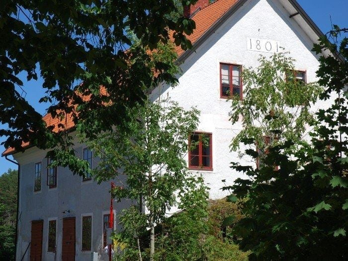 Whitewashed building with a red tiled roof and the year 1801, partially obscured by greenery.