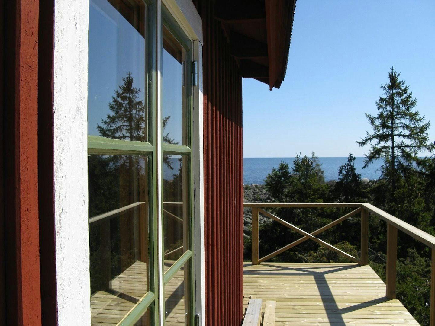 Balcony with sea view from a red cottage surrounded by pine trees.