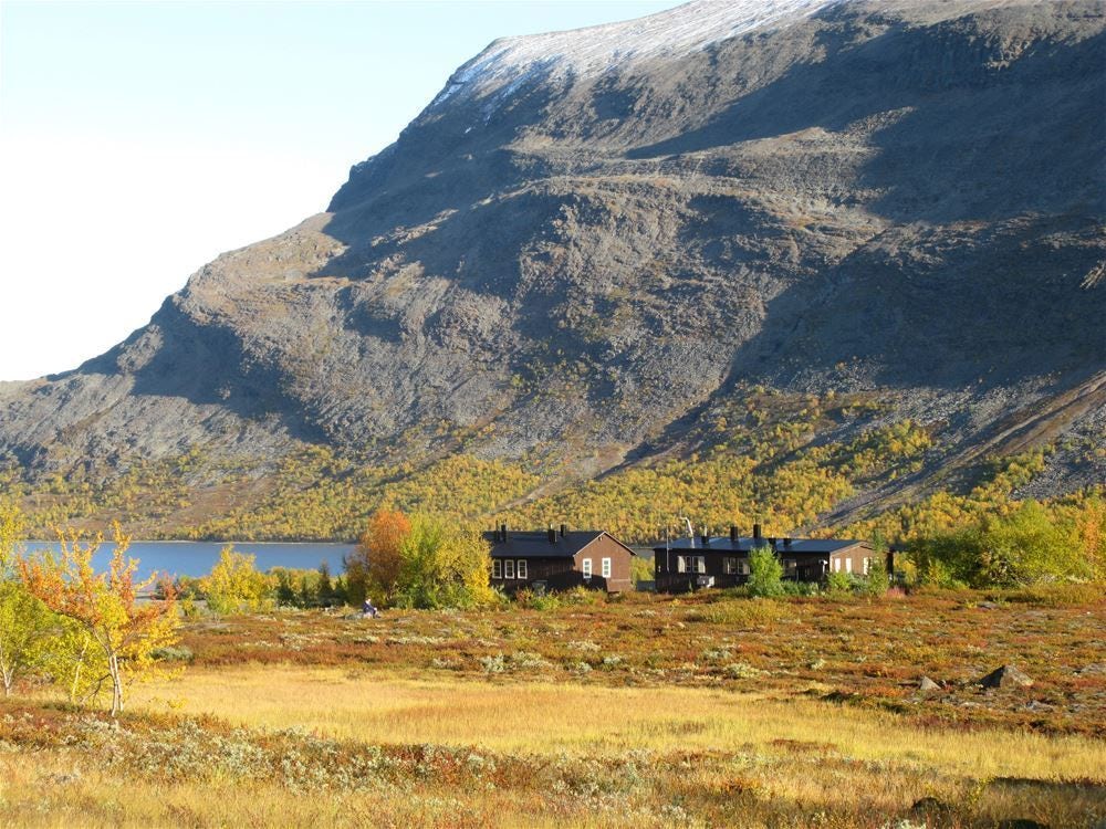 Fjällstugor vid foten av brant fjällsida i höstlandskap.