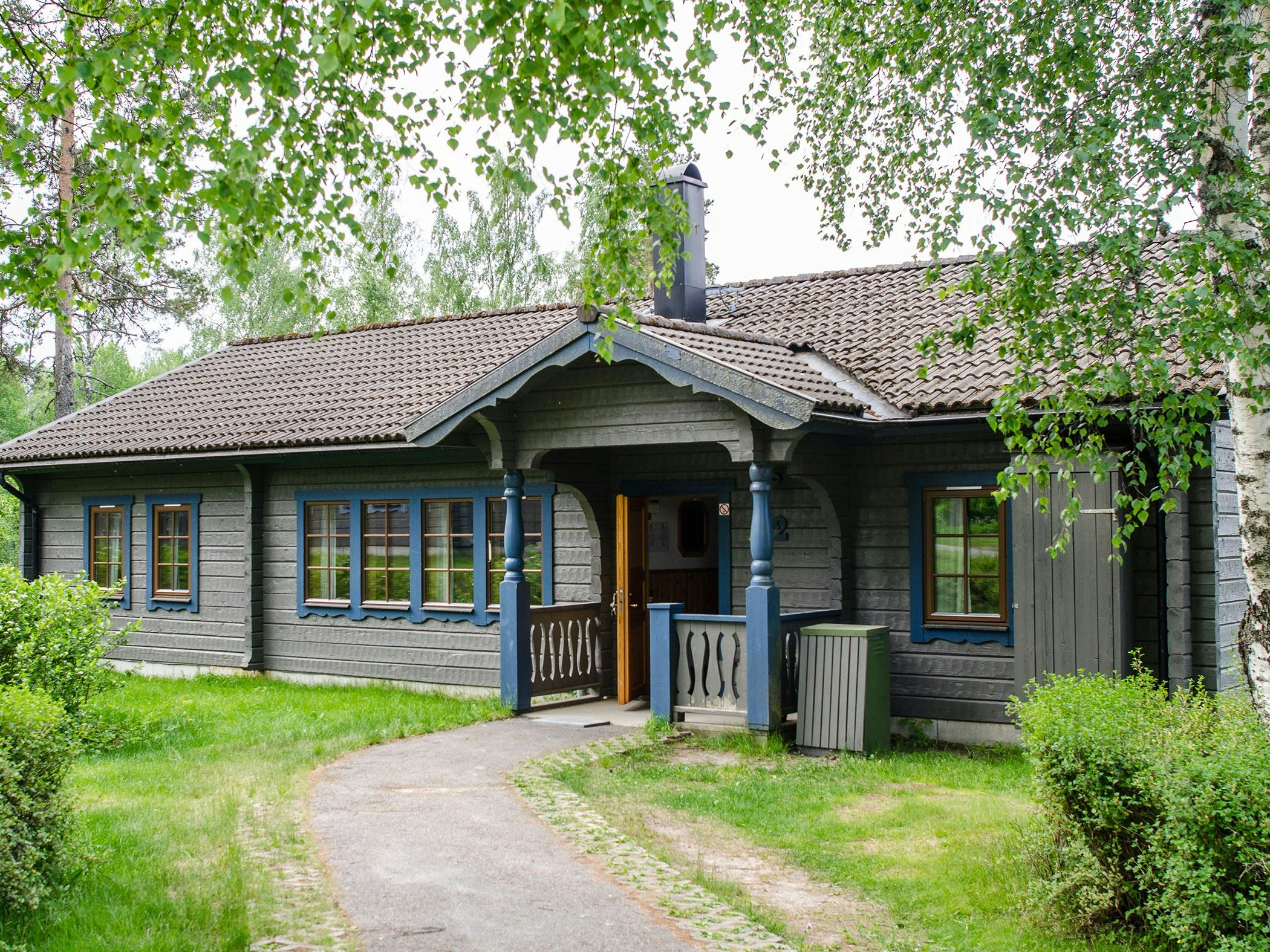 Gray log cabin with blue window details and open door in lush surroundings.