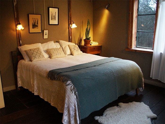 Mysigt sovrum med jordnära färger, dubbelsäng och varm belysning vid fönster.