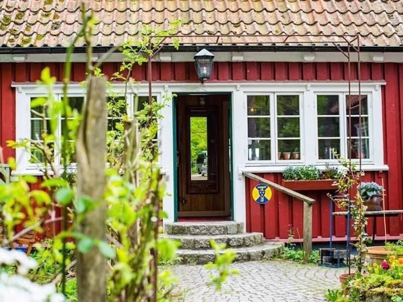 Red wooden villa with white painted windows, paved entrance and lush garden.